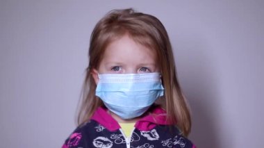 Mavi tıbbi maskeli küçük sarışın kız üzgün. Maskeyi çıkar. Pembe kazaklı. Covid 19 pandemia. Çocuklar karantinada. Tam HD görüntüler.