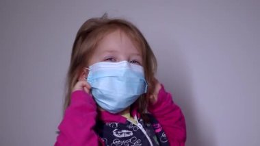 Mavi tıbbi maskeli küçük sarışın kız üzgün. Pembe kazaklı. Covid 19 pandemia. Çocuklar karantinada. Tam HD görüntüler.