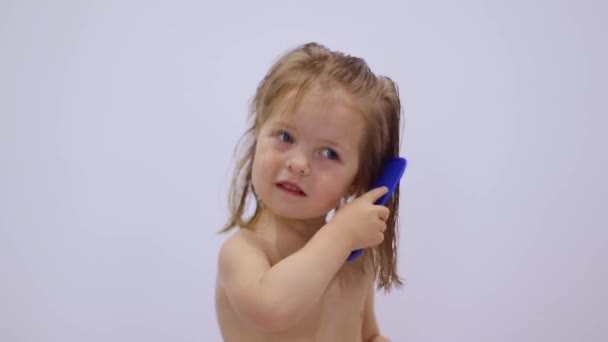흰 배경에 파란 빗으로 머리를 빗고 있는 귀여운 금발 소녀. 모발 관리. 자녀 양육. 독립. FullHD 영상 — 비디오