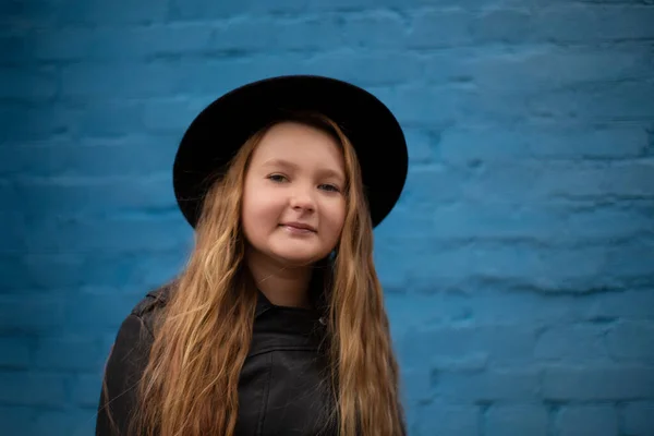 ブルーレンガの壁の背景に革のジャケットと黒の帽子でかわいいブルネットの10代の女の子の肖像画 ファッション スタイル — ストック写真