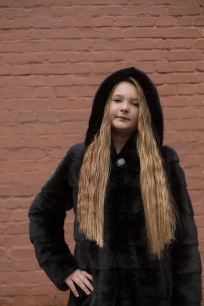 茶色のレンガの壁の背景に黒の毛皮のコートのかわいいブルネットの10代の女の子の肖像画 ファッション スタイル — ストック写真