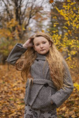 Gri montlu güzel esmer kızın sonbahar ormanındaki portresi. Sıcacık sonbahar.