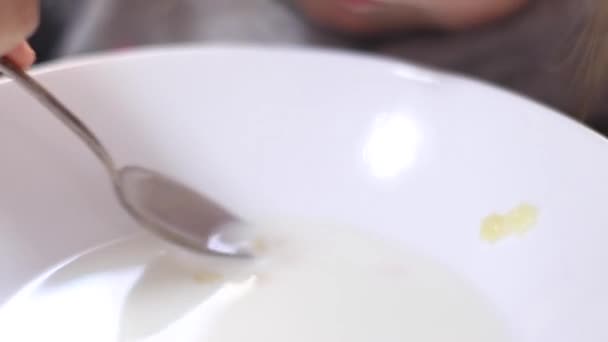 Jolie petite blonde en pyjama mangeant du porridge au lait avec des vermicelles d'astérisque. petit déjeuner, matin, à la maison. Vidéos en Full HD — Video