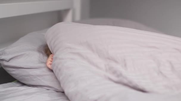 Mooi blond meisje spelen verstoppertje op grijs bed. Lachen, plezier hebben. Ochtendroutine, kindertijd, peuter, dochter. FullHD-beelden — Stockvideo
