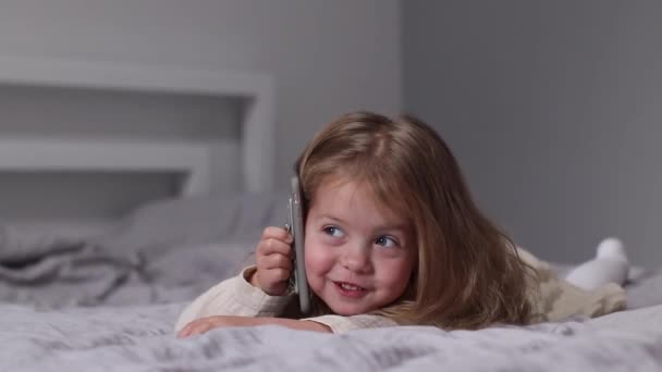 Ładna blondynka w sukience rozmawiająca przez telefon w szarej sypialni. poranna rutyna, dzieciństwo, maluch, córka. Nagrania w Full HD — Wideo stockowe