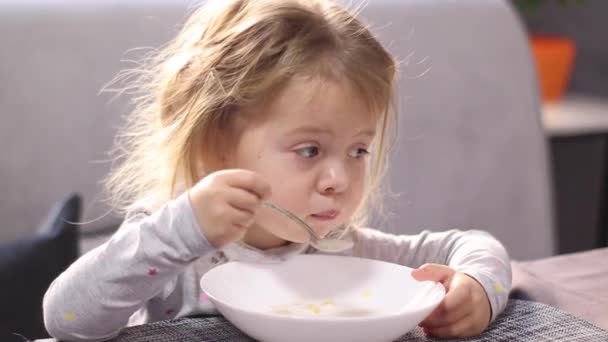 Pretty little blonde girl in pajama eating milk porridge with asterisk vermicelli. breakfast, morning, home. FullHD footage — Vídeos de Stock