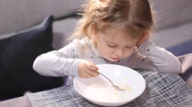 Pijamalı güzel sarışın kız yıldız vermicelli sütlü lapa yiyor. Kahvaltı, sabah, evde. Tam HD görüntüler