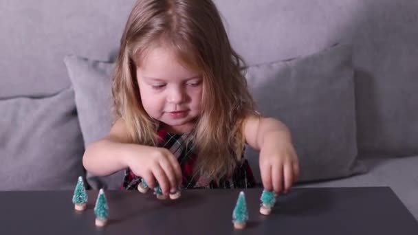 Mooi klein meisje spelen met kleine kerstbomen speelgoed, decoraties. Nieuwjaar, jeugd, dochter. FullHD-beelden — Stockvideo