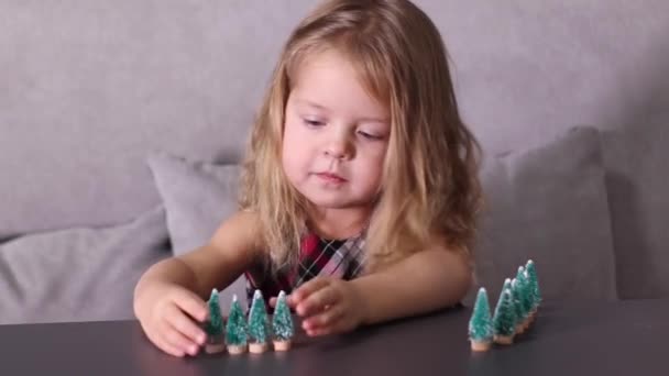 Hübsche kleine Mädchen spielen mit kleinen Weihnachtsbäumen Spielzeug, Dekorationen. Neues Jahr, Kindheit, Tochter. FullHD-Aufnahmen — Stockvideo