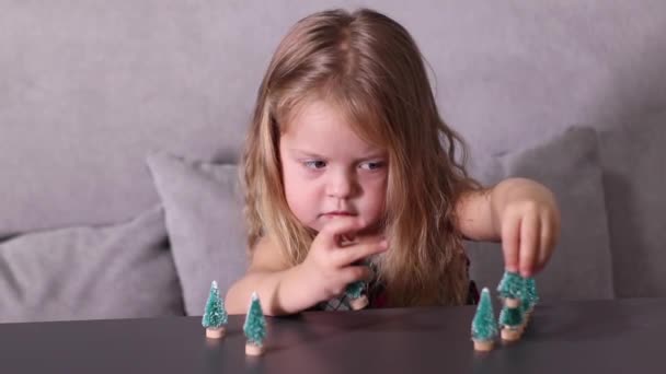Ładna dziewczynka bawiąca się małymi choinkami, zabawkami, dekoracjami. Nowy rok, dzieciństwo, córka. Nagrania w Full HD — Wideo stockowe