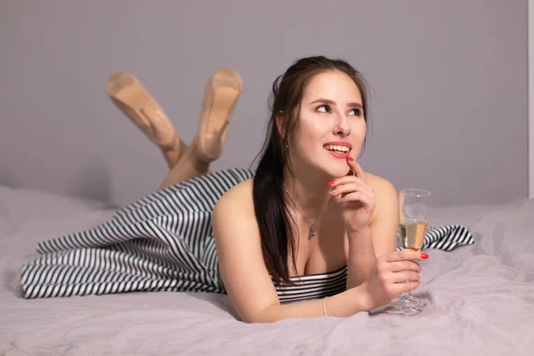 Счастливая Привлекательная Брюнетка Вечернем Коктейльном Платье Бокалом Шампанского Кровати Серой — стоковое фото