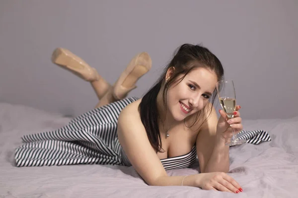 Счастливая Привлекательная Брюнетка Вечернем Коктейльном Платье Бокалом Шампанского Кровати Серой — стоковое фото