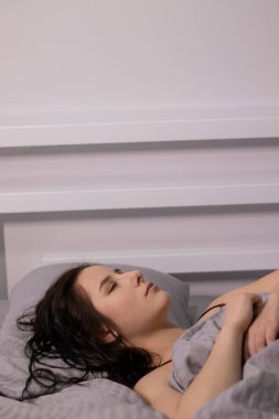 Yatakta gri çarşafların altında bordo bluzlu esmer kız. Sabah rutini. rüya, uyku. Boşluğu kopyala