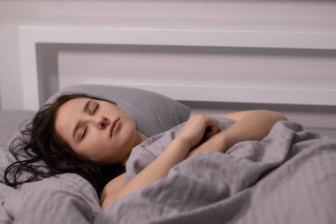 Yatakta gri çarşafların altında bordo bluzlu esmer kız. Sabah rutini. rüya, uyku. Boşluğu kopyala