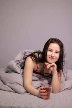 Yatağında cam bardak çay ve gri çarşaflı çekici, esmer kadın. Sabah rutini. Boşluğu kopyala