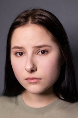 Gri arka planda, bataklık rengi tişörtlü, çekici, üzgün esmer kadın portresi. Oyunculuk, duygu. Boşluğu kopyala