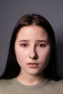 Gri arka planda, bataklık rengi tişörtlü, çekici, üzgün esmer kadın portresi. Oyunculuk, duygu. Boşluğu kopyala