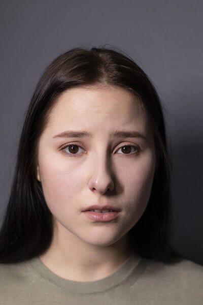 portrait of charming sad brunette woman in marsh color t-shirt on grey wall background. actress acting, emotion. copy space