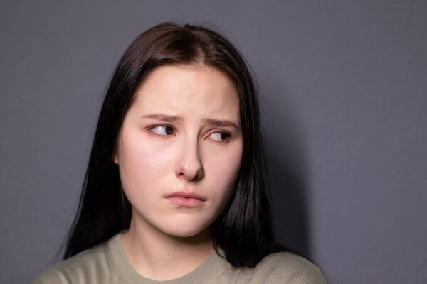 portrait of charming sad brunette woman in marsh color t-shirt on grey wall background. actress acting, emotion. copy space