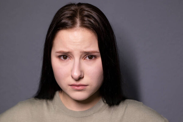 portrait of charming sad brunette woman in marsh color t-shirt on grey wall background. actress acting, emotion. copy space