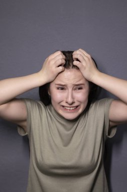 Gri arka planda, bataklık rengi tişörtlü çekici, korkmuş esmer kadın portresi. Oyunculuk, duygu. Boşluğu kopyala