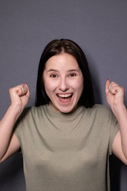 Gri arka planda, bataklık rengi tişörtlü çekici, esmer kadın portresi. Oyunculuk, duygu. Boşluğu kopyala