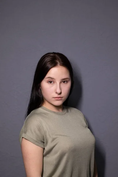 灰色の壁の背景に湿地色のTシャツの魅力的なブルネットの女性の感情的な肖像画 女優の演技感情 コピースペース — ストック写真