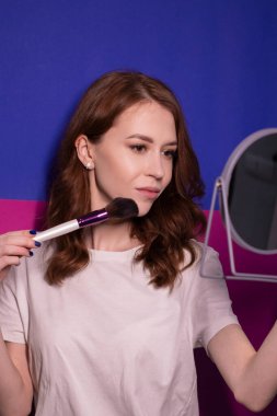 Makyaj fırçaları renkli mavi ve pembe arka planda olan beyaz tişörtlü çekici esmer kadın. Profesyonel makyöz. Boşluğu kopyala