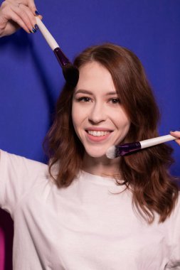 Makyaj fırçaları renkli mavi arka planda olan beyaz tişörtlü çekici esmer kadın. Profesyonel makyöz. Boşluğu kopyala