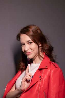 Kırmızı deri ceketli çekici esmer kadın makyaj fırçaları gri duvar arkasında izole edilmiş. Profesyonel makyöz. Boşluğu kopyala