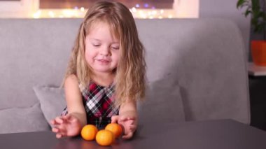 Gri odada Mandarin Clementine olan kırmızı kareli elbiseli sevimli küçük kız. Yeni yıl, çocukluk, Noel. Tam HD görüntü.