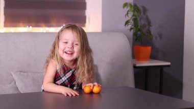 Gri odada Mandarin Clementine olan kırmızı kareli elbiseli sevimli küçük kız. Yeni yıl, çocukluk, Noel. Tam HD görüntü.