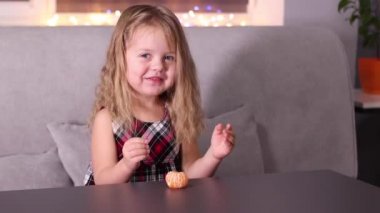 Gri odada Mandarin Clementine olan kırmızı kareli elbiseli sevimli küçük kız. Yeni yıl, çocukluk, Noel. Tam HD görüntü.