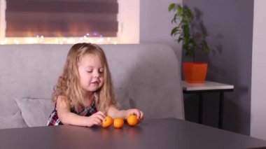 Gri odada Mandarin Clementine olan kırmızı kareli elbiseli sevimli küçük kız. Yeni yıl, çocukluk, Noel. Tam HD görüntü.