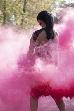 Siyah elbiseli, parlak pembe duman bombasıyla tanınmayacak kadar zayıf esmer bir kız. Dans etmek, eğlenmek. renk pudrası İlkbahar, yaz, sonbahar. Yüksek kalite fotoğraf