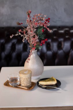 Süslü kırmızı dallı vazonun yanında bir fincan kahve ya da kapuçino. İç mekan, rahat. Boşluğu kopyala