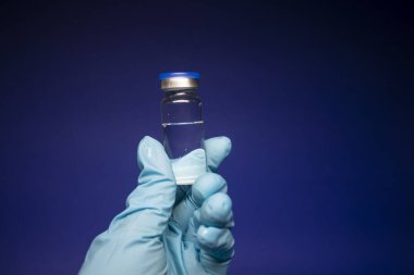 Koronavirüs aşısı COVID-19 'un gelişimi. Mavi tıbbi eldivende etiketi olmayan şişe şişesi. Mavi arka planda izole edilmiş. Tedavi. kopyalama alanı. Enfeksiyonların önlenmesi ve tedavisi için aşı