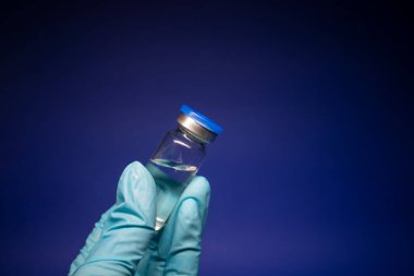 Koronavirüs aşısı COVID-19 'un gelişimi. Mavi tıbbi eldivende etiketi olmayan şişe şişesi. Mavi arka planda izole edilmiş. Tedavi. kopyalama alanı. Enfeksiyonların önlenmesi ve tedavisi için aşı