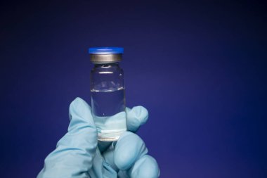 Koronavirüs aşısı COVID-19 'un gelişimi. Mavi tıbbi eldivende etiketi olmayan şişe şişesi. Mavi arka planda izole edilmiş. Tedavi. kopyalama alanı. Enfeksiyonların önlenmesi ve tedavisi için aşı