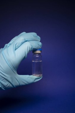 Koronavirüs aşısı COVID-19 'un gelişimi. Mavi tıbbi eldivende etiketi olmayan şişe şişesi. Mavi arka planda izole edilmiş. Tedavi. kopyalama alanı. Enfeksiyonların önlenmesi ve tedavisi için aşı