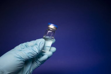 Koronavirüs aşısı COVID-19 'un gelişimi. Mavi tıbbi eldivende etiketi olmayan şişe şişesi. Mavi arka planda izole edilmiş. Tedavi. kopyalama alanı. Enfeksiyonların önlenmesi ve tedavisi için aşı