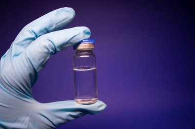 Koronavirüs aşısı COVID-19 'un gelişimi. Mavi tıbbi eldivende etiketi olmayan şişe şişesi. Mavi arka planda izole edilmiş. Tedavi. kopyalama alanı. Enfeksiyonların önlenmesi ve tedavisi için aşı