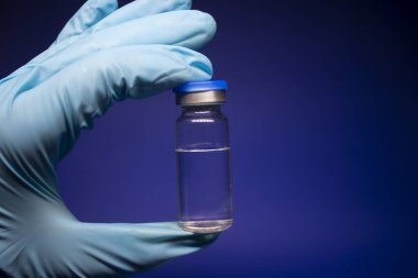 Koronavirüs aşısı COVID-19 'un gelişimi. Mavi tıbbi eldivende etiketi olmayan şişe şişesi. Mavi arka planda izole edilmiş. Tedavi. kopyalama alanı. Enfeksiyonların önlenmesi ve tedavisi için aşı