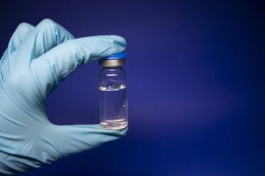 Koronavirüs aşısı COVID-19 'un gelişimi. Mavi tıbbi eldivende etiketi olmayan şişe şişesi. Mavi arka planda izole edilmiş. Tedavi. kopyalama alanı. Enfeksiyonların önlenmesi ve tedavisi için aşı