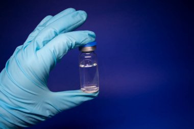 Koronavirüs aşısı COVID-19 'un gelişimi. Mavi tıbbi eldivende etiketi olmayan şişe şişesi. Mavi arka planda izole edilmiş. Tedavi. kopyalama alanı. Enfeksiyonların önlenmesi ve tedavisi için aşı