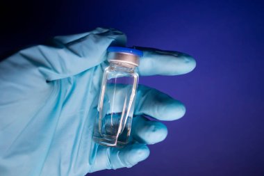 Koronavirüs aşısı COVID-19 'un gelişimi. Mavi tıbbi eldivende etiketi olmayan şişe şişesi. Mavi arka planda izole edilmiş. Tedavi. kopyalama alanı. Enfeksiyonların önlenmesi ve tedavisi için aşı