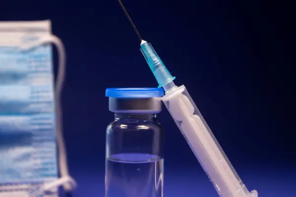 在蓝色医疗面罩和注射针注射器附近没有标签的疫苗瓶状药瓶 被蓝色背景隔离 Coronavirus疫苗Covid 19的开发 复制空间 — 图库照片