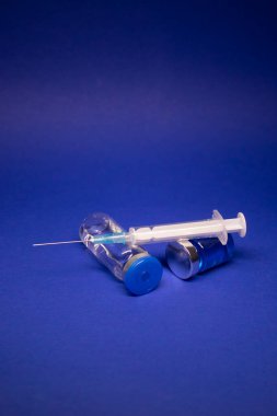 Etiketsiz iki şeffaf aşı şişesi şırınga iğnesi. Mavi arka planda izole edilmiş. Koronavirüs aşısı COVID-19 'un gelişimi. Araştırmada dünya yarışı. Boşluğu kopyala
