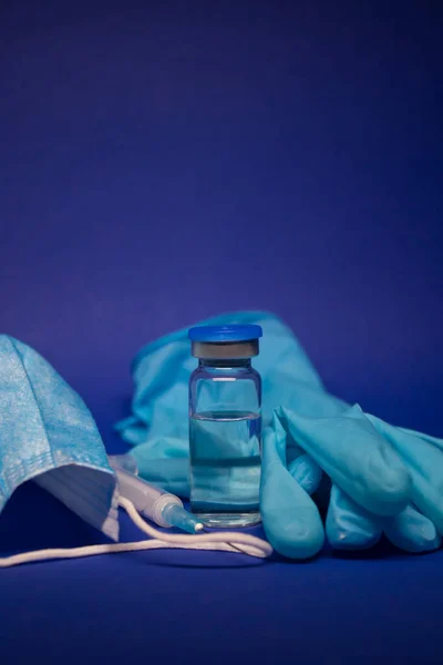 Vaccine bottle phial with no label, medical syringe with injection needle, blue medical mask and gloves . isolated on blue background. cure. Development of coronavirus vaccine COVID-19. copy space