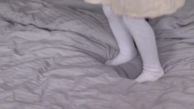 Güzel küçük kız eğleniyor, gri yatak odasında yatağa atlıyor. Sabah rutini, çocukluk, kız. Tam HD görüntüler